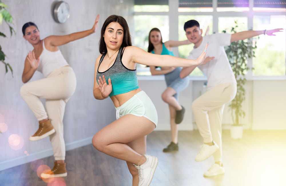 Brunette teenage girl practicing vigorous dance with group in studio