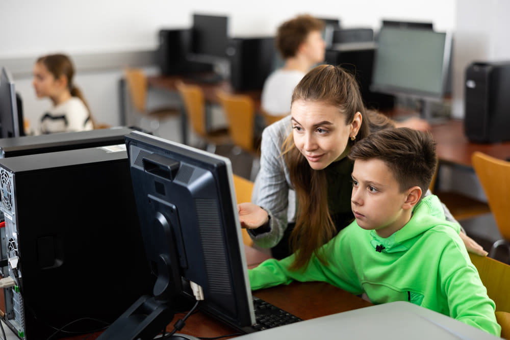 Female teacher helping focused preteen schoolboy studying in computer lab