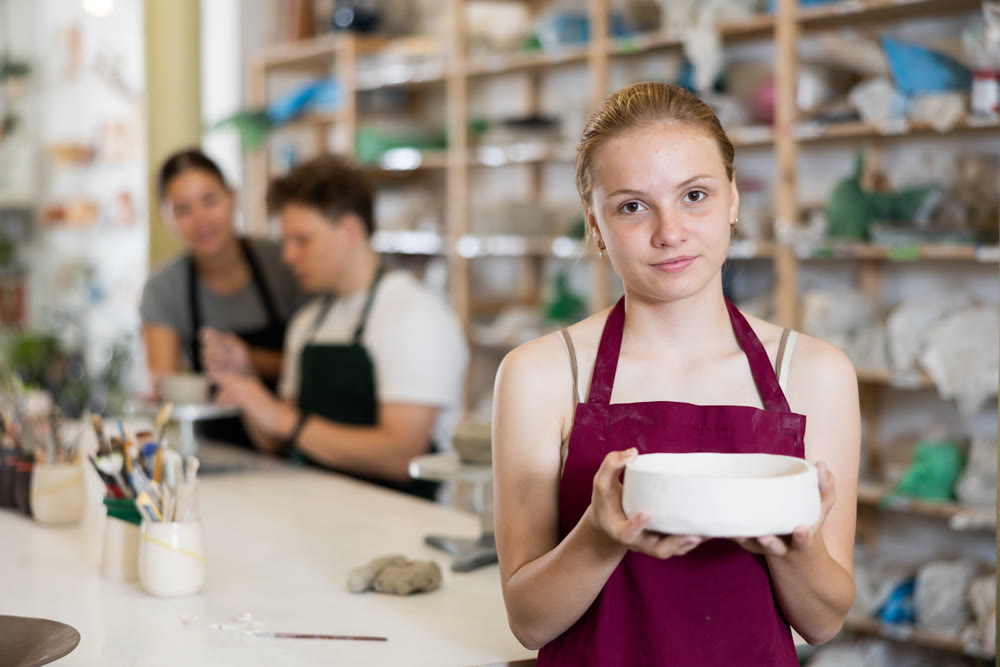 Teenage girl posing with ceramic bowl in ceramic workshop