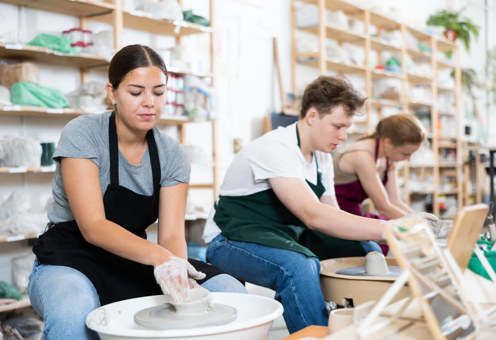Female artisan in ceramics workshop with pottery wheel and various clay vessels