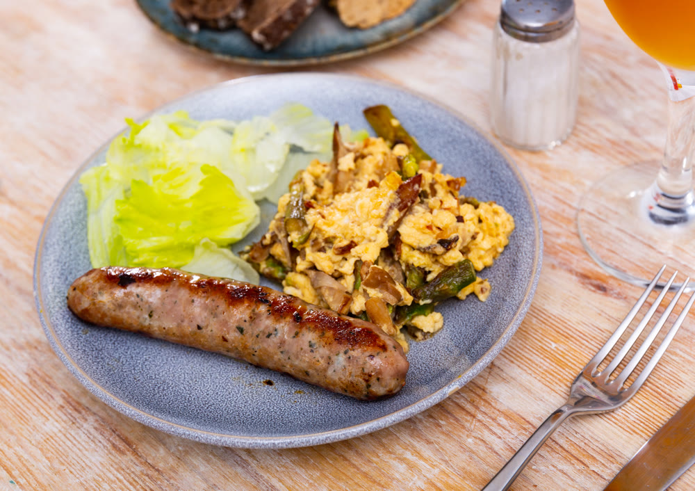 Scrambled eggs with mushrooms, chicken fillet and asparagus with sausages are served on plate