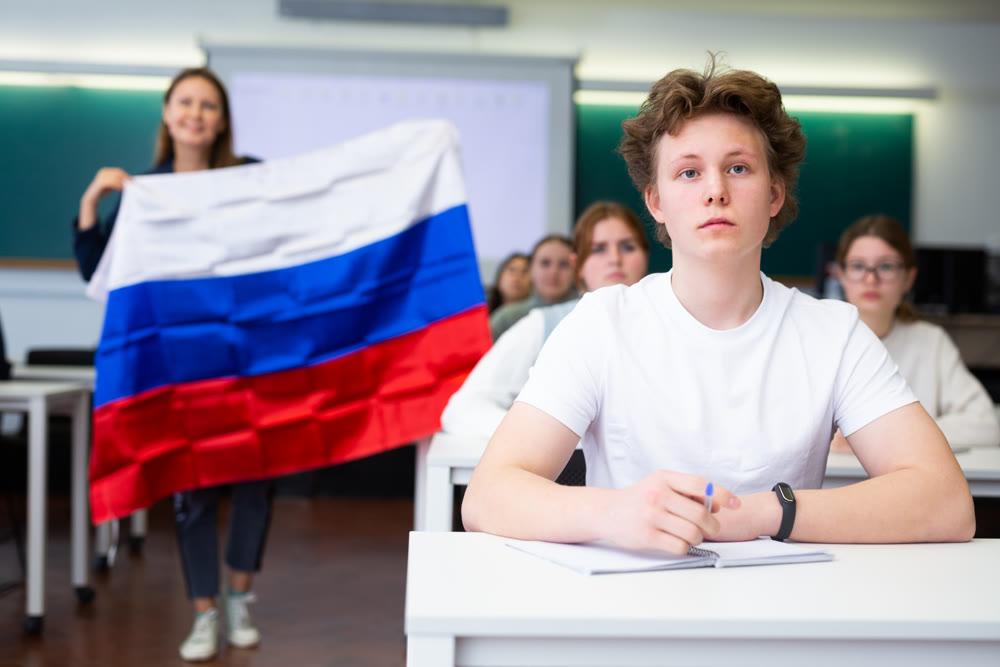 Female teacher tells her classmates about the country of Russian, holding flag in her hands