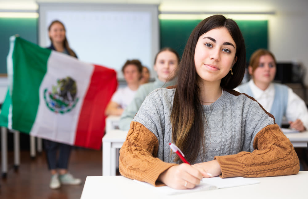 Female teacher tells her classmates about the country of Mexico, holding a flag in hands