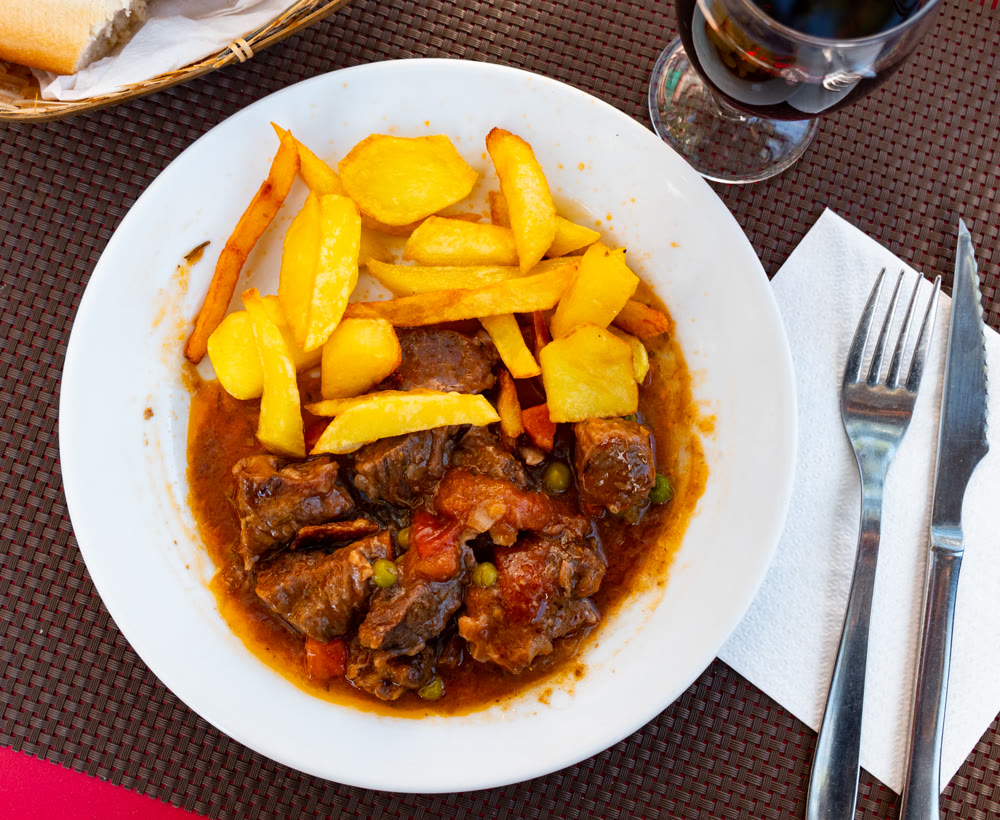 Juicy veal stew in tomato red sauce with green pea, garnished with French fries