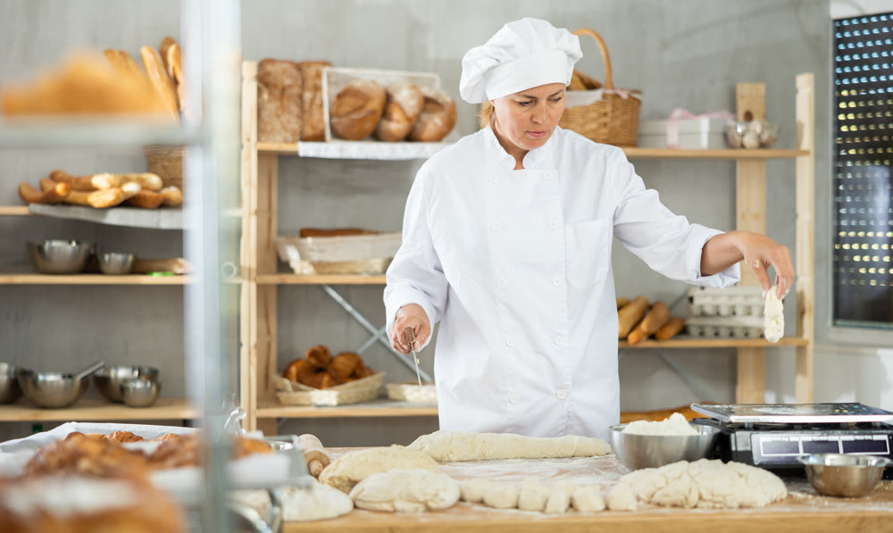 Female cook is working with dough, weighing piece of dough on scale.