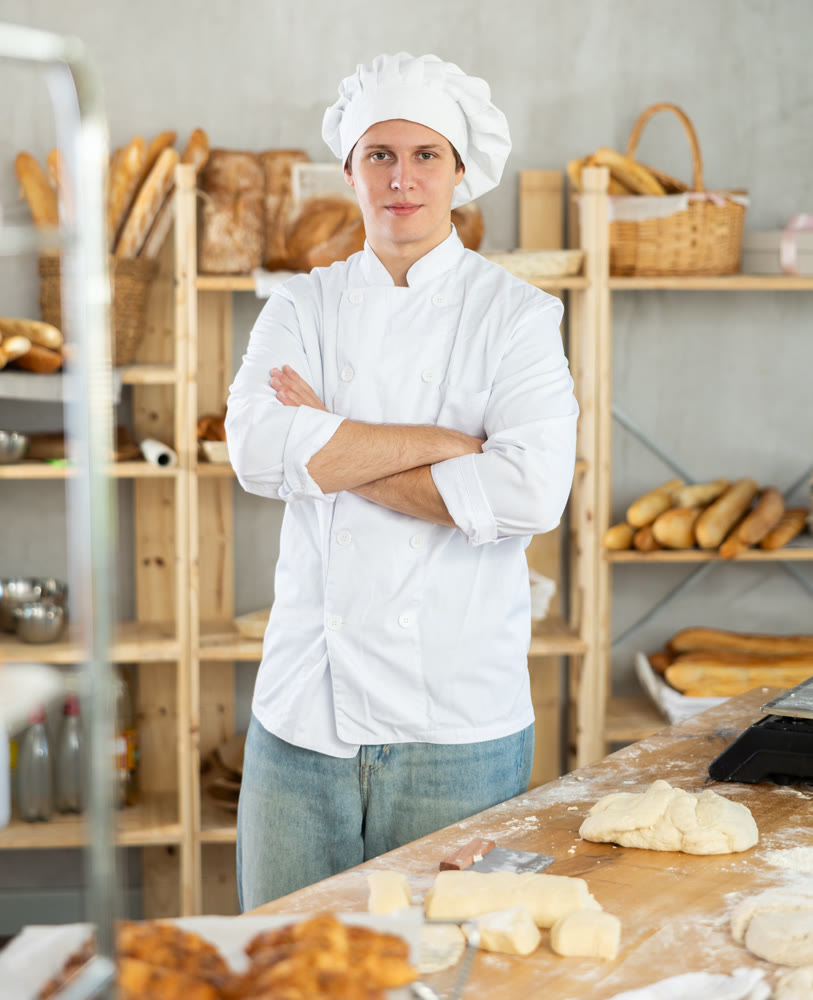 Portrait of young man baker smiling at camera posing during daily work in bakery