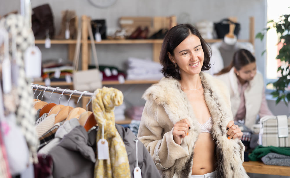 Woman try on fur jacket in front of mirror in clothes store, semi naked body