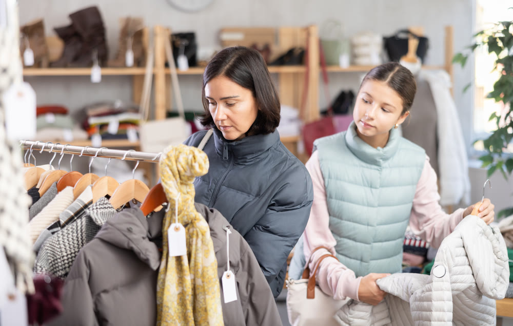 Mother and teen daughter looks at products in store and selects coat or jacket for child