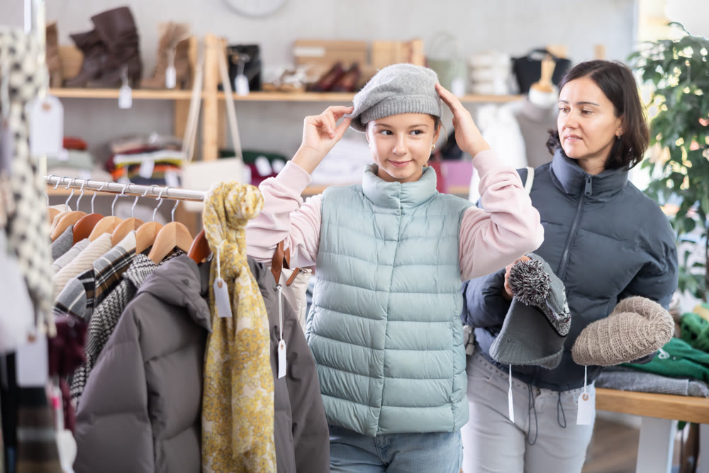 Adolescence girl try on hat during shopping with mother in clothes store, family shopping with mom