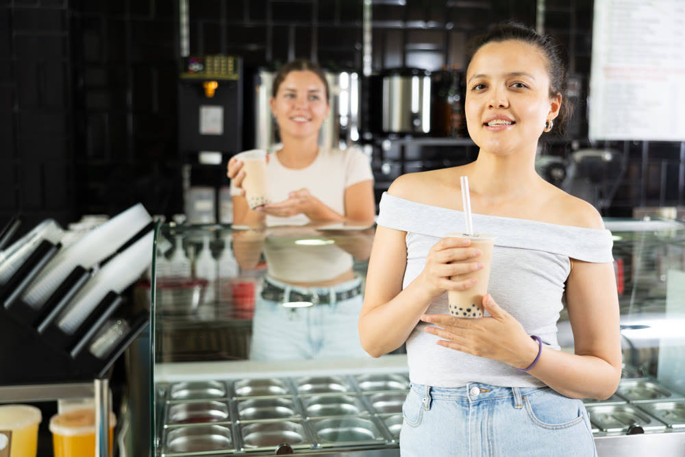 Satisfied joyful asian girl drinking tea with bubble milk in cafe