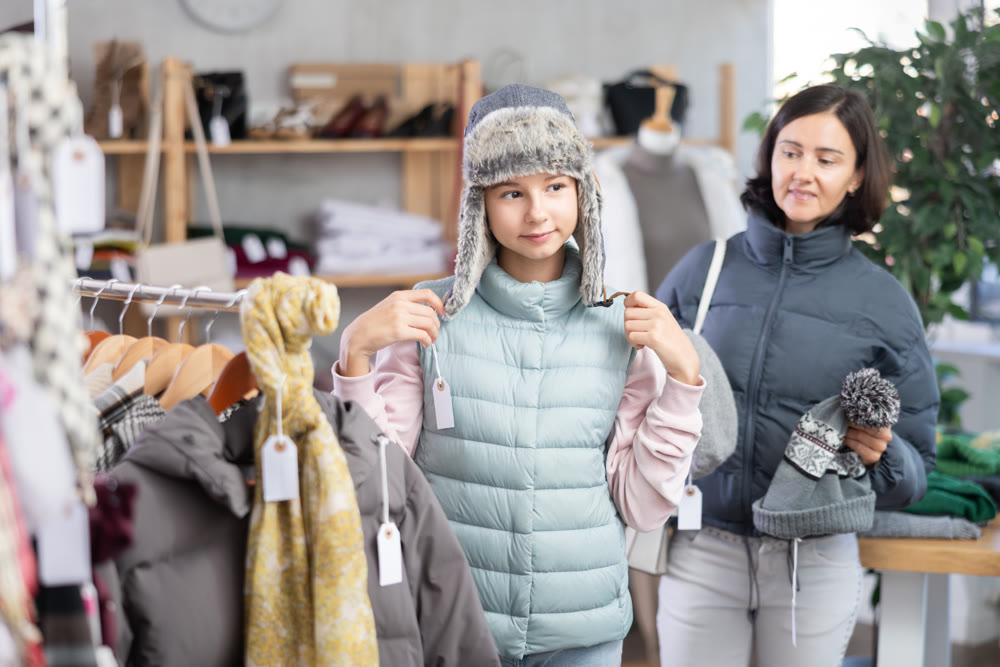 Teenage girl with her mother try on fur hat in store