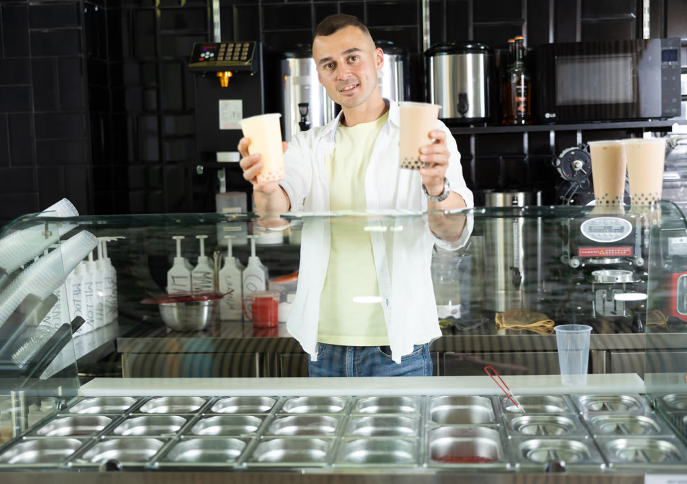 Seller handing disposable cups of refreshing bubble tea to customer