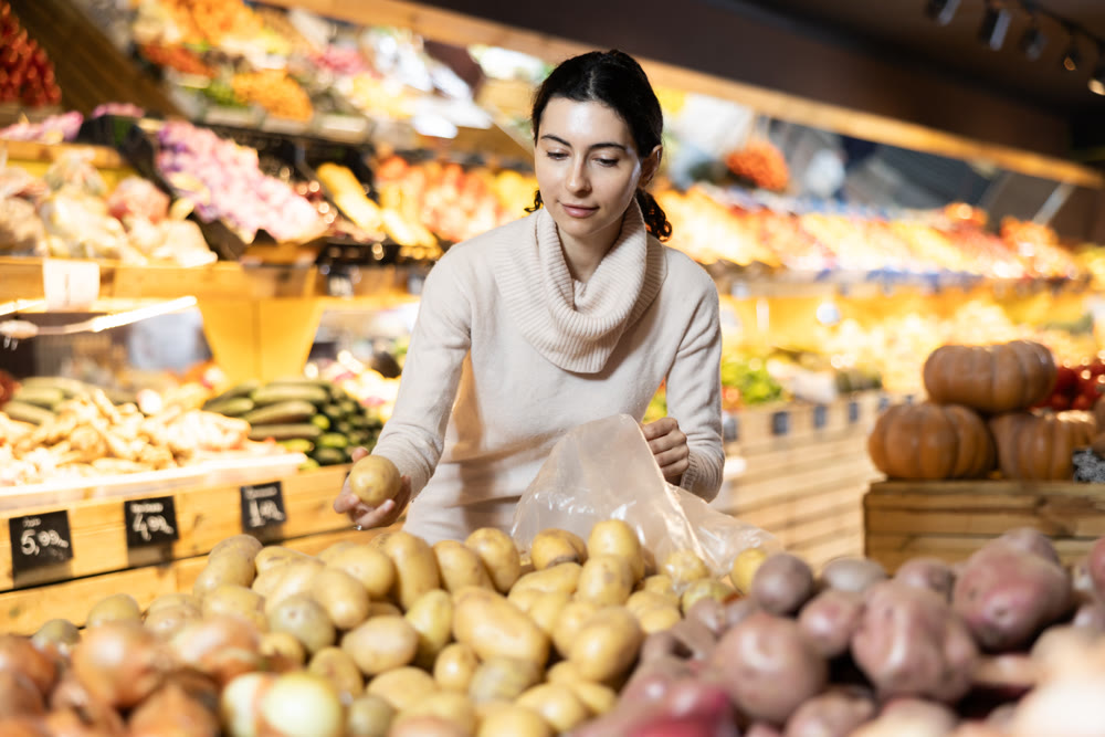 In vegetable store, young woman customer buy ripe potato
