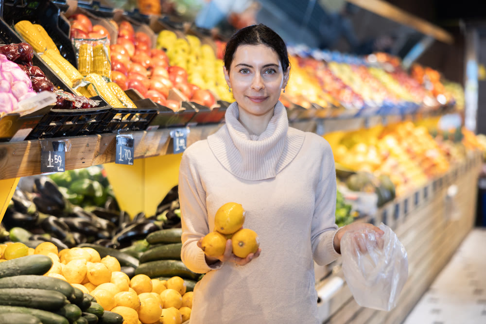Young woman chooses lemons in vegetable shop