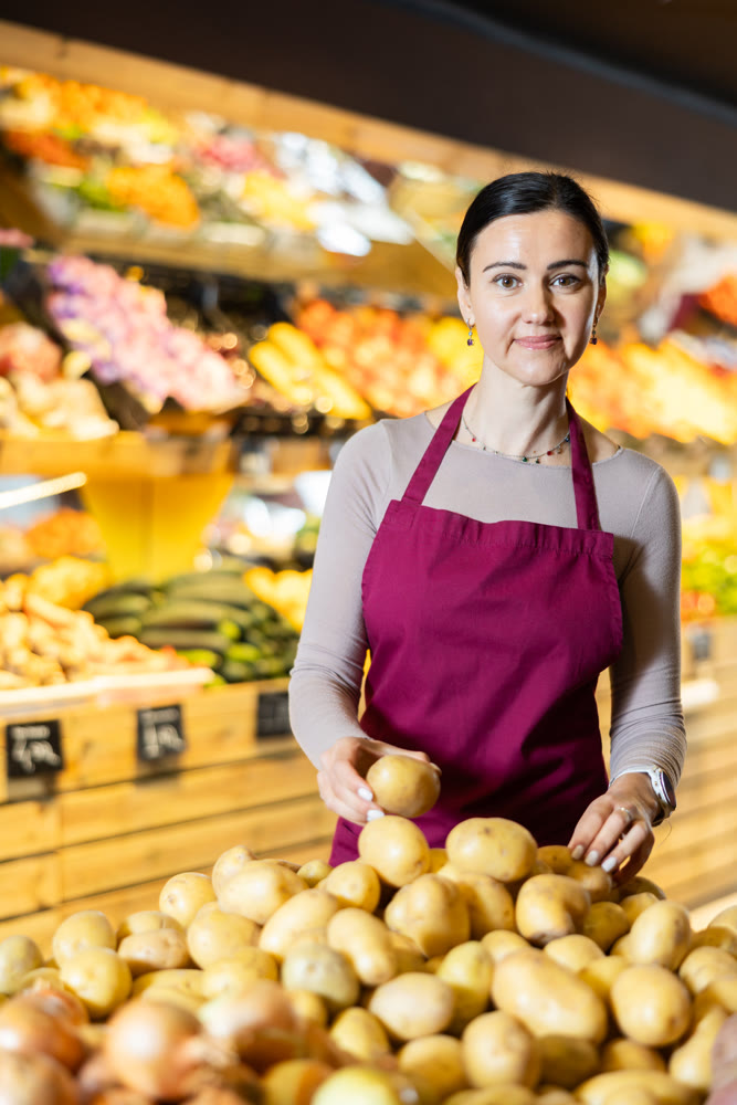 Supermarket female worker inspects vegetables, checks the quality of potatoes, rearranges products and sets up display case