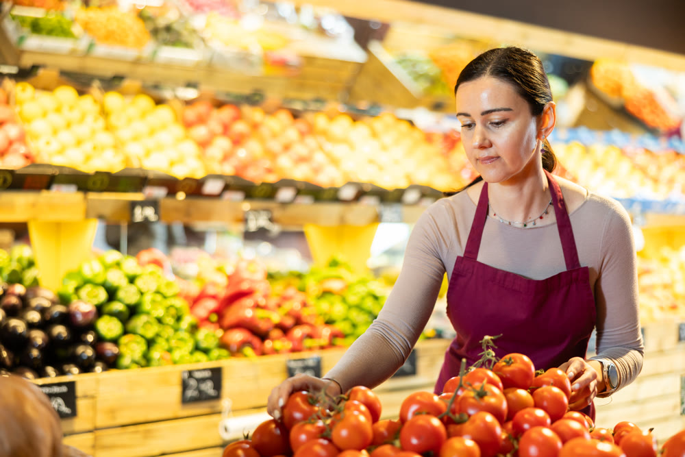 Middle-aged female seller putting tomatoes on counter in grocery market