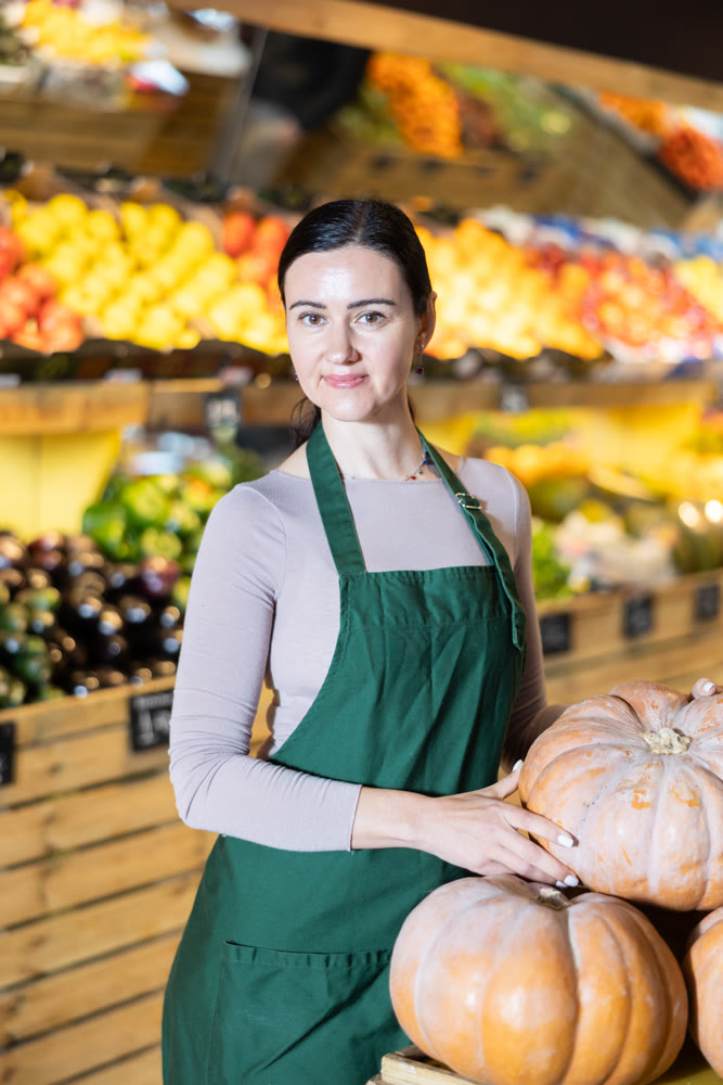 Middle-aged female seller offering pumpkin in grocery market