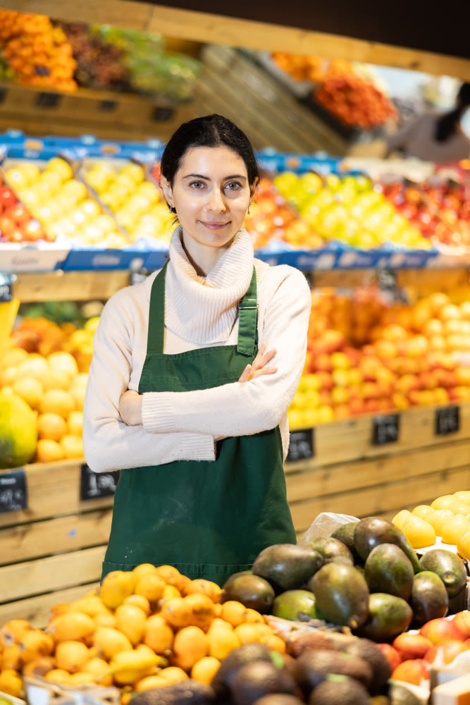 Young woman seller offering avocado in vegetable shop