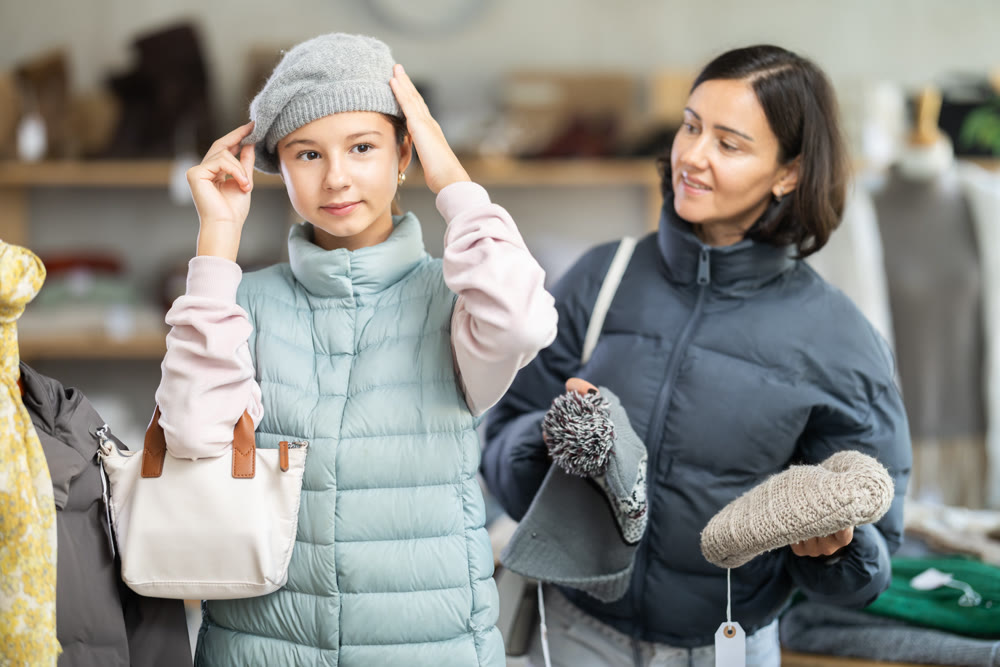 Teenage girl with her mother try on hat in store