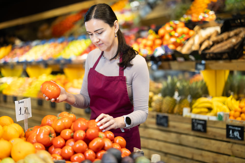 Supermarket employee carefully places ripe tomatoes on shelves of grocery supermarket