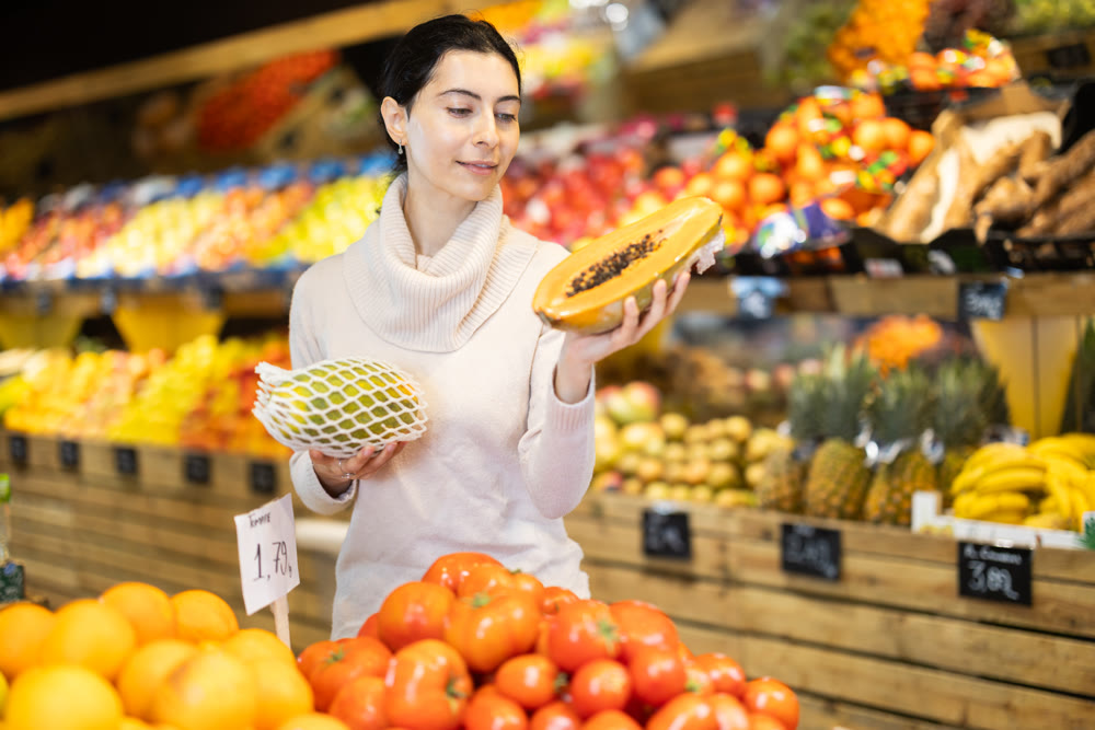 Young woman choosing papaya at vegetable shop