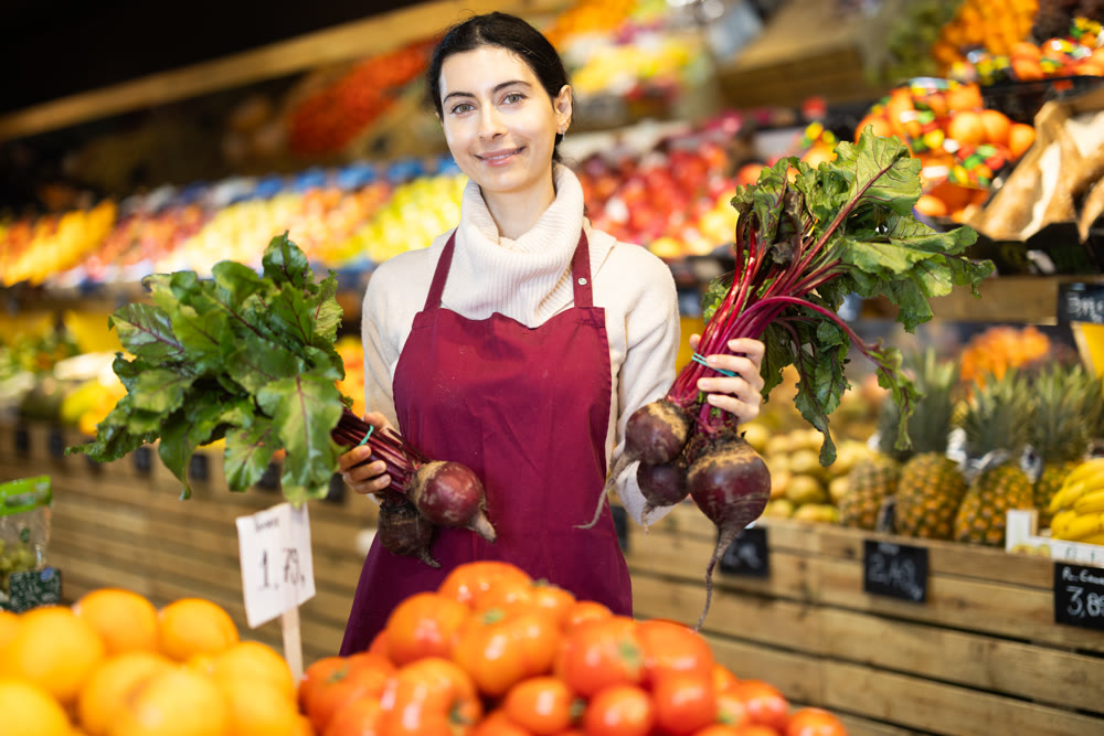 Young woman seller offering beets in vegetable shop