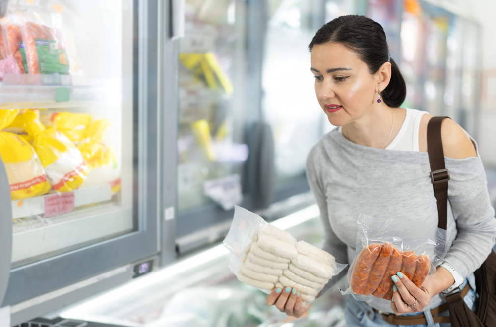 Woman in supermarket choose cooled raw sausages