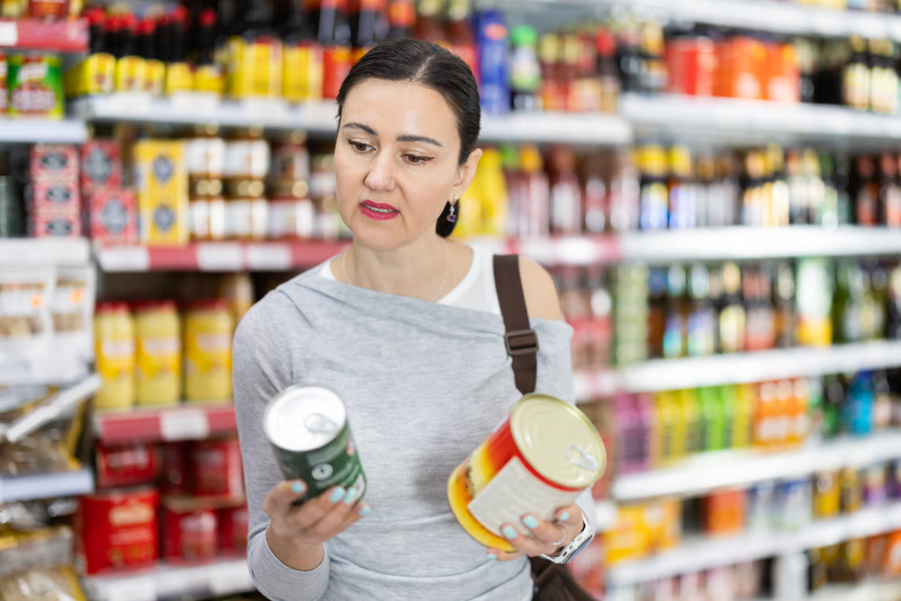 Woman customer in supermarket choose canned food, buy food stuff in grocery store