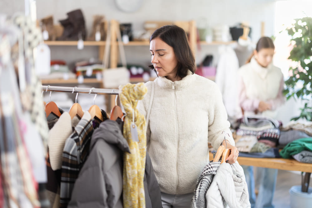 Adult woman chooses coat or down jacket in clothing store