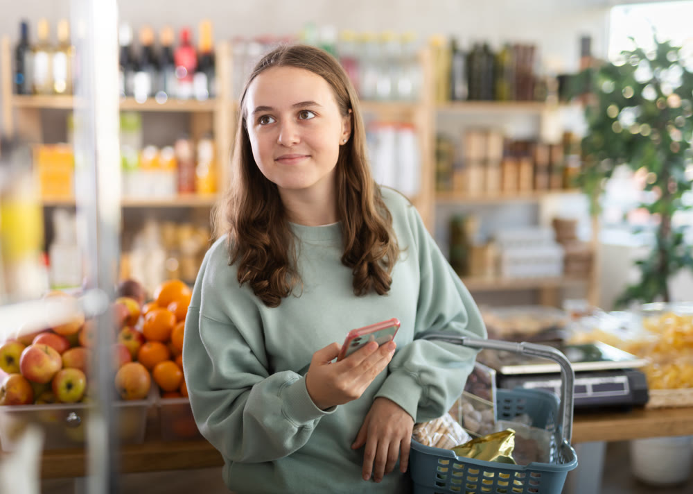 Visiting store, teen girl with phone is looking at something on shelf of showcase.