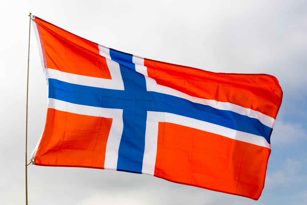 Against background of cloudy sky, Norwegian flag flapping in wind on flagpole