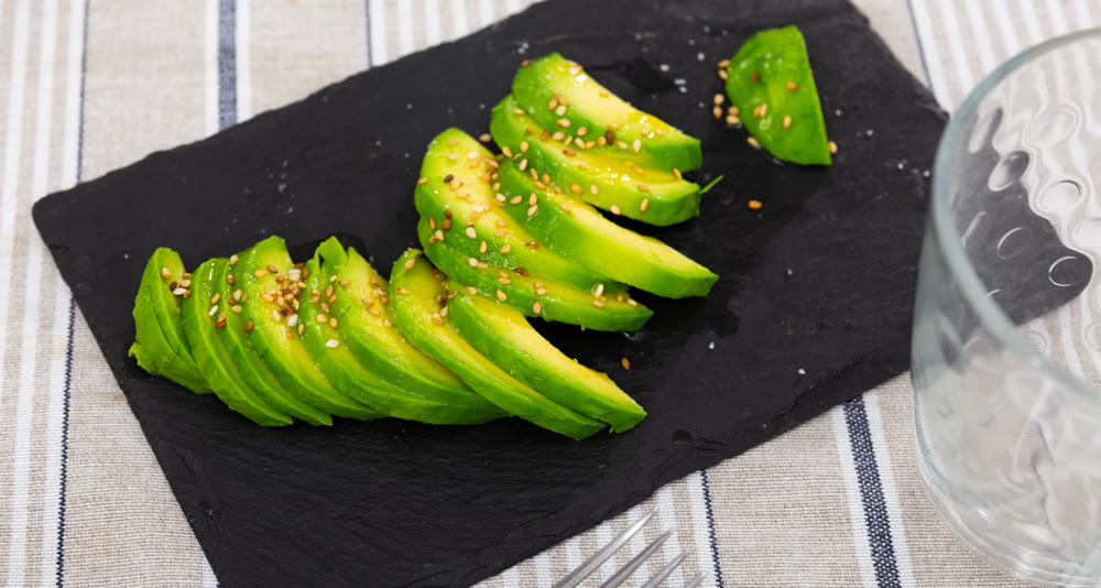 On table there is plate with snack -pieces of avocado pulp.