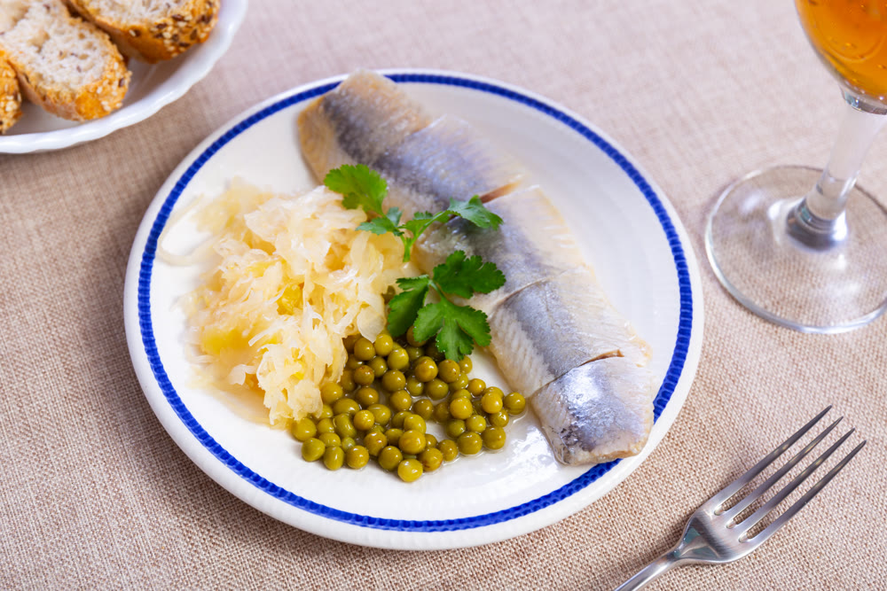 Tasty slices herring fish with canned green peas, pickled cabbage, decorated by onion rings served on plate