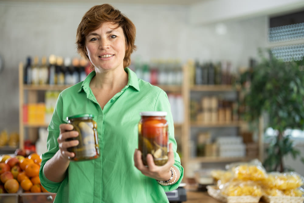 Female shopper selects pickled tomatoes in the produce section of supermarket