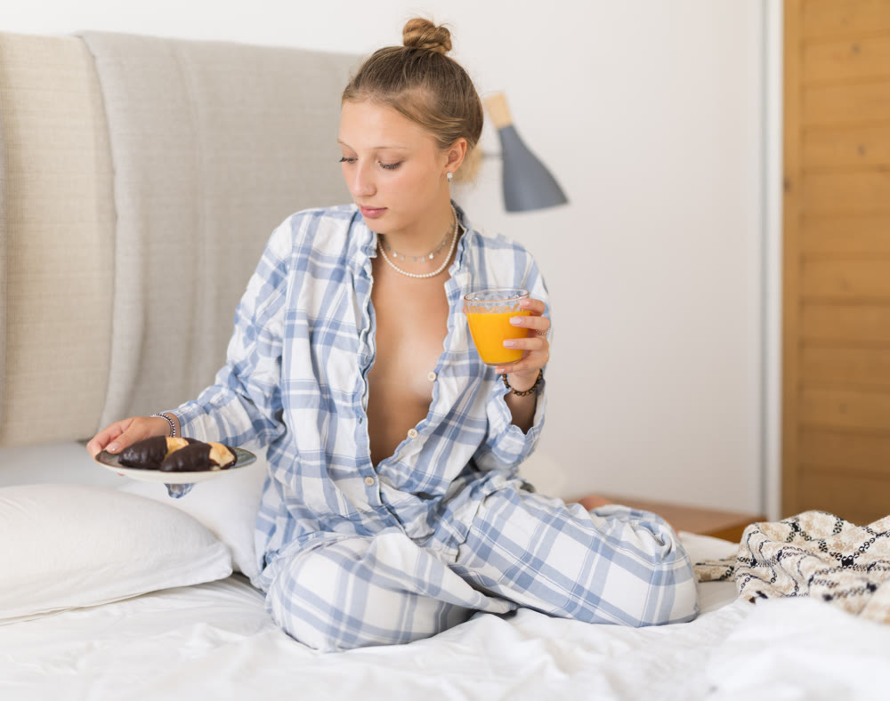 Breakfast in bed - young girl in pajamas drinking juice and eating cookies while sitting on bed in bedroom