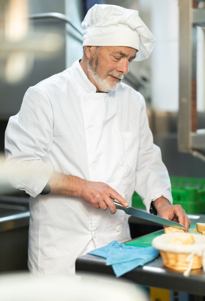 Senior man cook in kitchen finely slices food