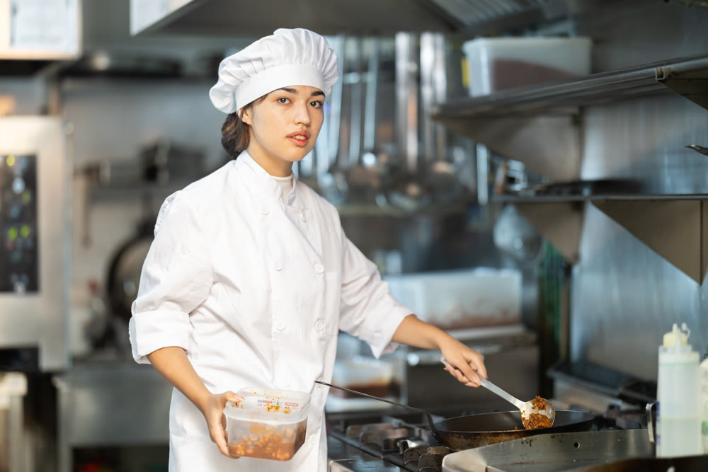 Young female chef prepares dish in frying pan