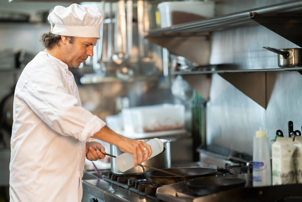 Adult male chef prepares dish in frying pan