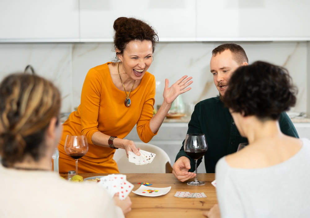 Friendly company of men and women sitting at kitchen table and enjoying the poker game. Friends play a card game at home. Evening entertainment concept