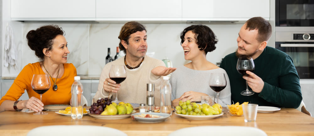 Group of happy celebrating holiday drinking and chatting at table at kitchen
