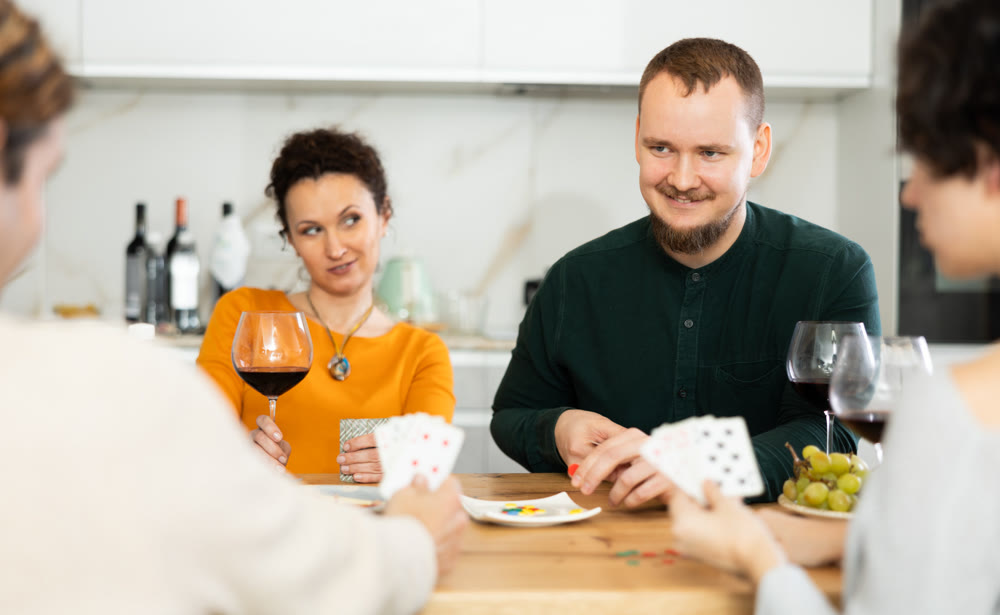 Happy group of friends playing poker cards and drinking wine