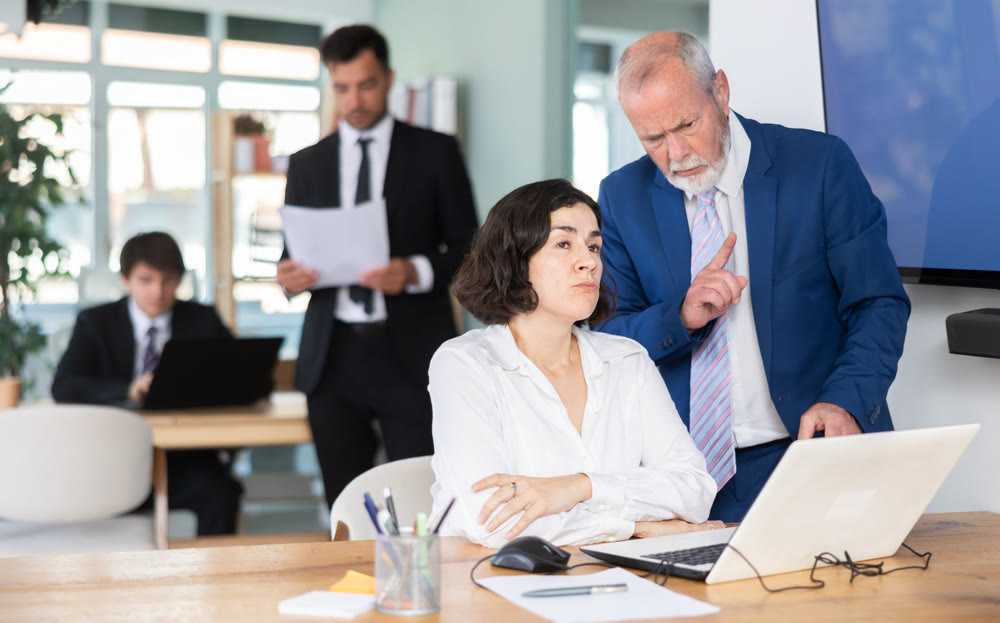 Strict mature man boss scolding girl office worker for improper operation on laptop in office