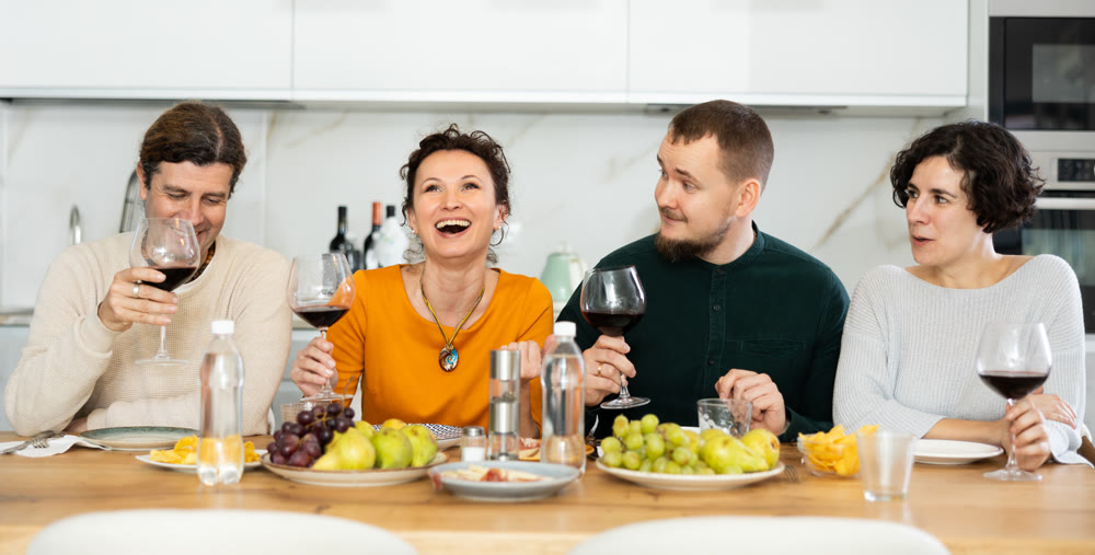 Two married couples are sitting at table, enjoying food and wine, chatting, talking, laughing.