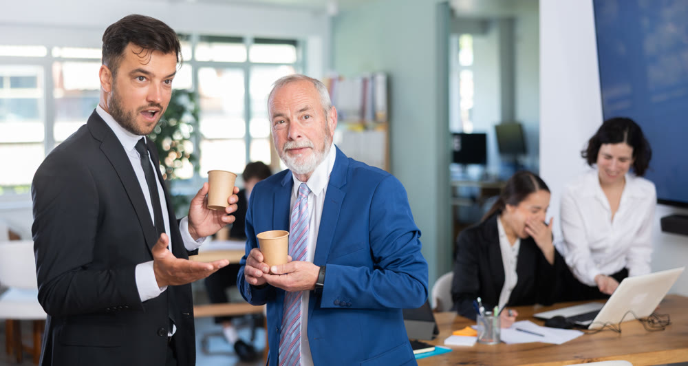 Elderly and adult male colleagues drinking coffee in office