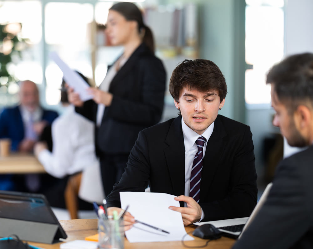 Experienced young male bank manager talking with adult man client and helping opening account in bank at office