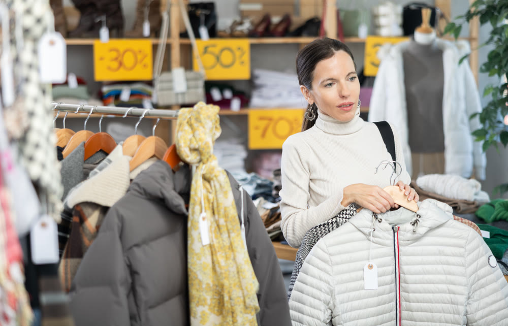 Woman chooses fashionable down jacket in clothing boutique