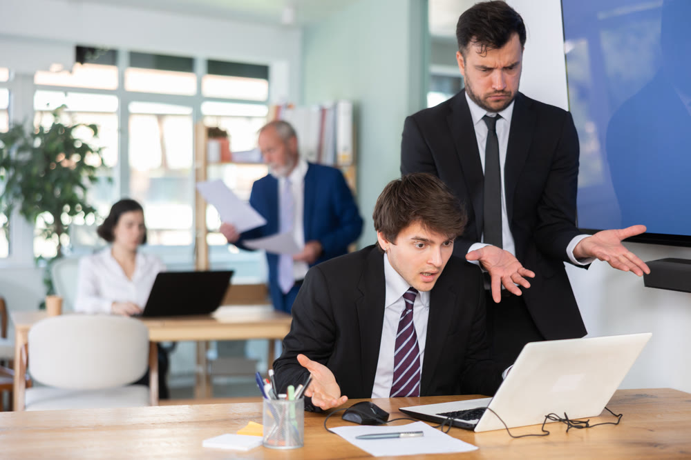 Dissatisfied adult male senior manager scolding new young guy office worker for improper operation on laptop in office