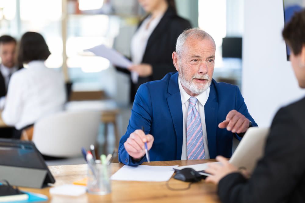 Experienced mature male bank manager talking with man client and helping opening account in bank at office