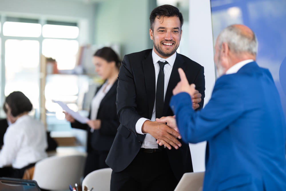 Adult bank manager shaking hands with elderly male client