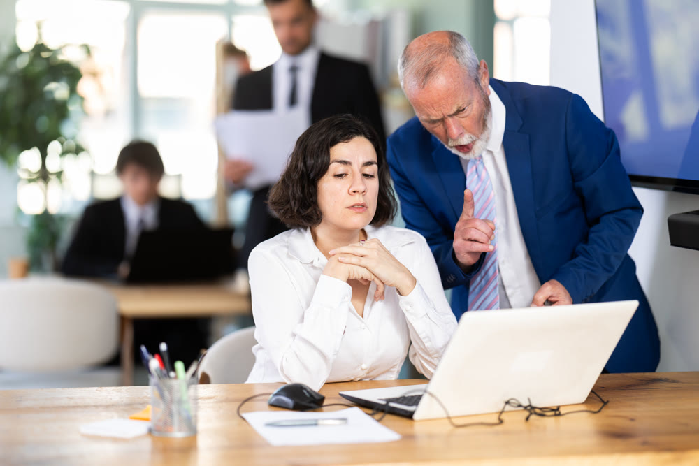 Strict mature man boss scolding girl office worker for improper operation on laptop in office